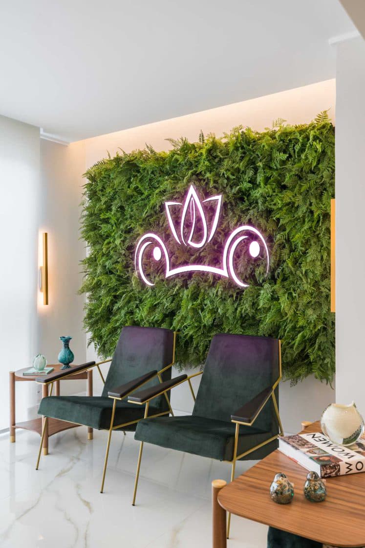 Sala de espera da Liftam com parede de folhagem viva e o logo em neon rosé